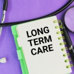 Notebook labeled “Long Term Care” with a stethoscope, pen, and magnifying glass, representing a glossary term for long-term care insurance