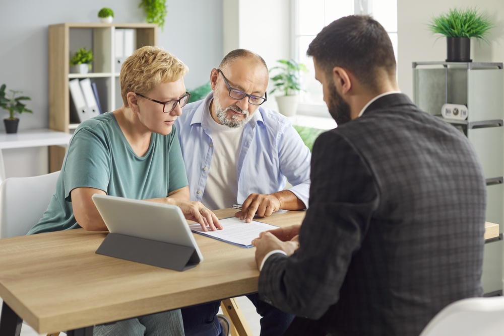 A couple at retirement age, reviewing insurance contract with a lawyer across a desk.